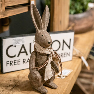 Textured rabbit sculpture sitting upright on a wooden shelf in a styled retail setting.