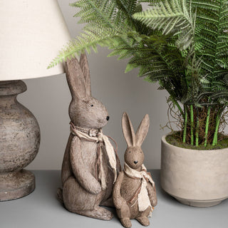 Small rabbit sculpture displayed next to a larger matching rabbit, a lamp, and a potted fern plant.