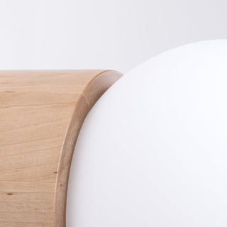 Close-up of the smooth junction between the light maple wood base and the opaque white glass sphere.