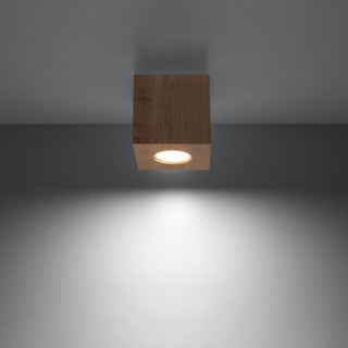 Wooden quad ceiling lamp switched on, showing the warm white light beam projecting onto a wall.