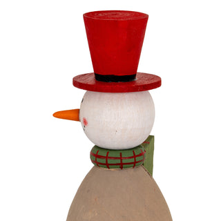 Close-up profile view of the wooden snowman's head, showing the red top hat, carrot nose, and green checked scarf.
